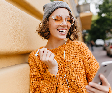 Smiling woman with smartphone and earbud outdoors